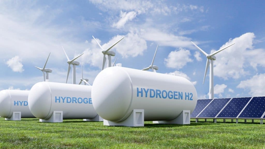 Weiße Lagertanks mit der Aufschrift Hydrogen H2 werden von nahegelegenen Windturbinen und Solaranlagen auf einem hellen, grasbewachsenen Feld versorgt.